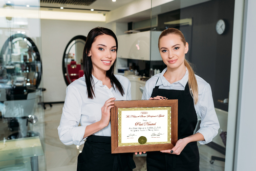 Two beauty professionals holding an education certification